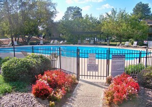 Une piscine privée, entourée d’une clôture, et bordée d’une végétation luxuriante et de fleurs rouges.