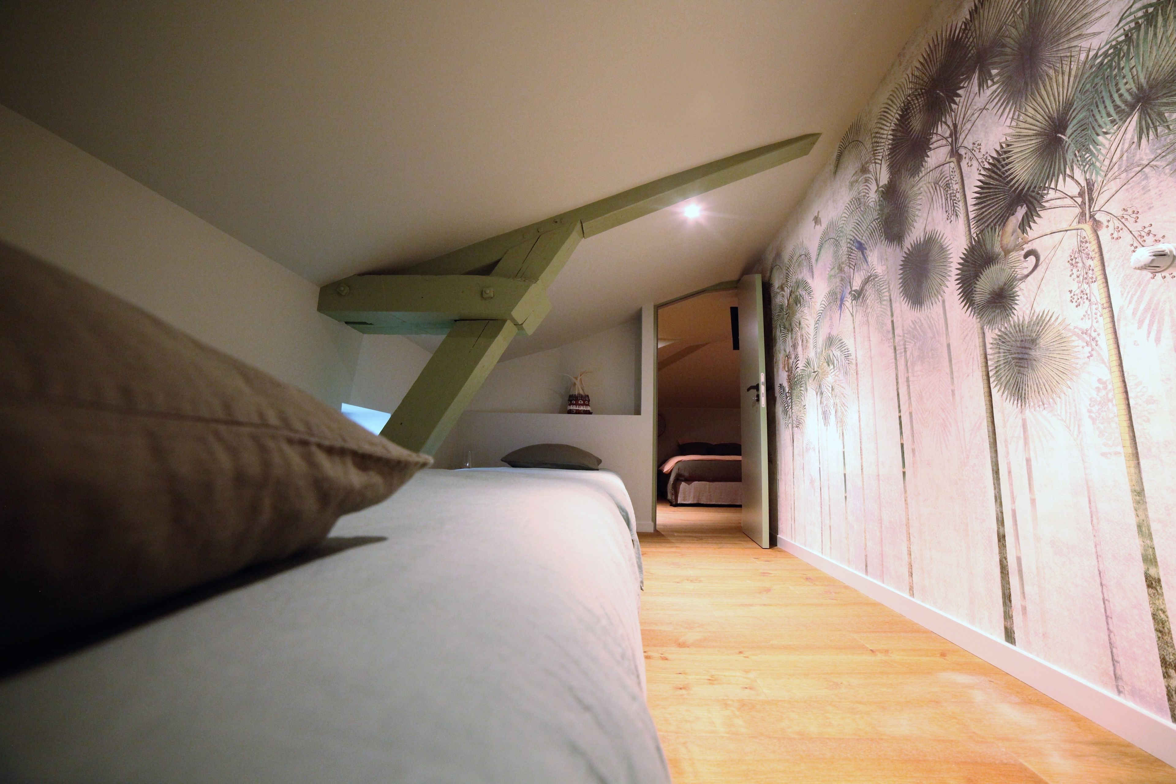 Une chambre avec un plafond en pente, un lit avec des oreillers, un plancher en bois et un mur orné d’une fresque florale.