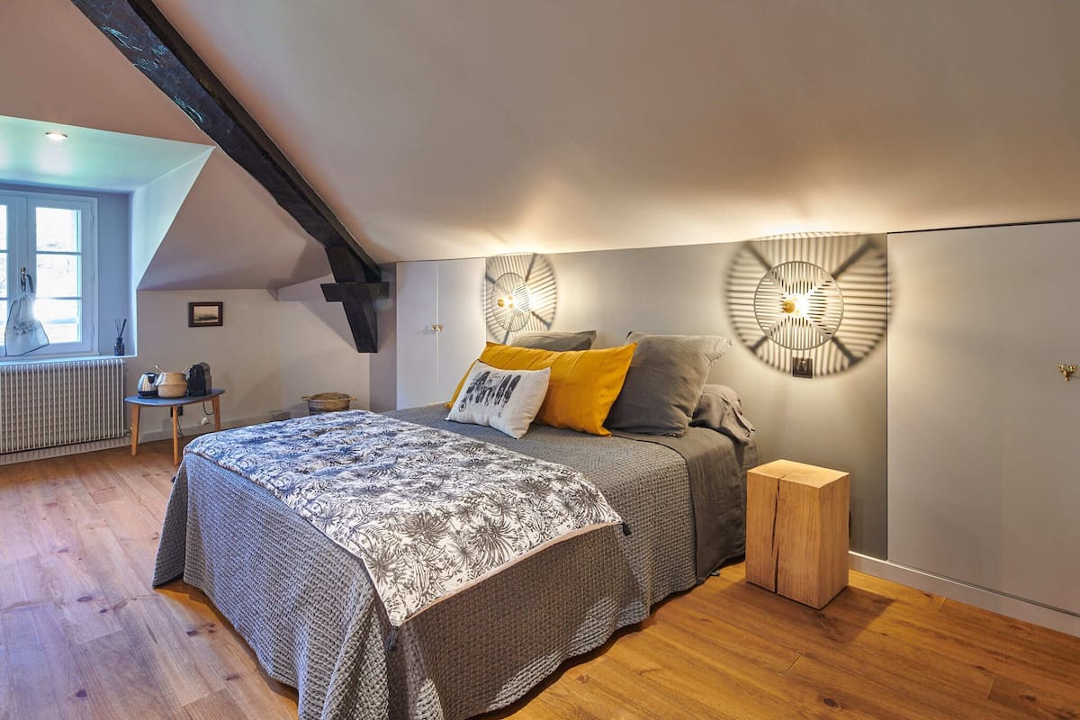 A bedroom with a sloped ceiling, a bed with patterned bedding, a small wooden nightstand, and wall-mounted lighting fixtures.