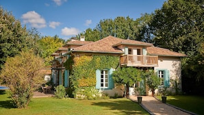 A two-story house with a tiled roof, green shutters, and a garden with a pathway leading to the entrance. - Bel Air Maison D'hôtes des Landes (Castets)