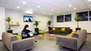 A modern waiting area with grey sofas, a TV, and potted plants.
