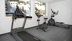 A gym with treadmills, an elliptical, and a stationary bike, with large windows offering a view of a snowy mountain and buildings.