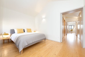 A modern bedroom with a bed, bedside table, lamp, and a view into an adjacent room. - Bom JardimApartments (Porto)