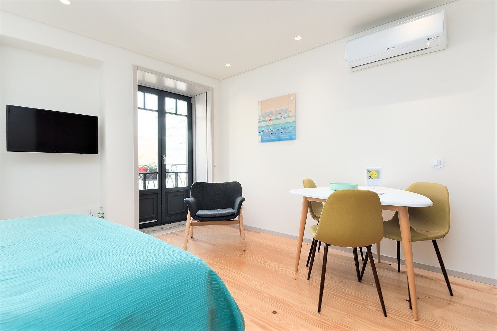 Een moderne kamer met een bed, een zithoek met stoelen, een aan de muur bevestigde televisie en een airconditioning.