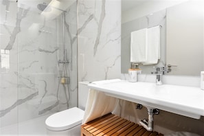 A modern bathroom with a glass-enclosed shower, a white toilet, a wooden bench, a white sink with a mirror, and a towel rack. - Bom JardimApartments (Porto)