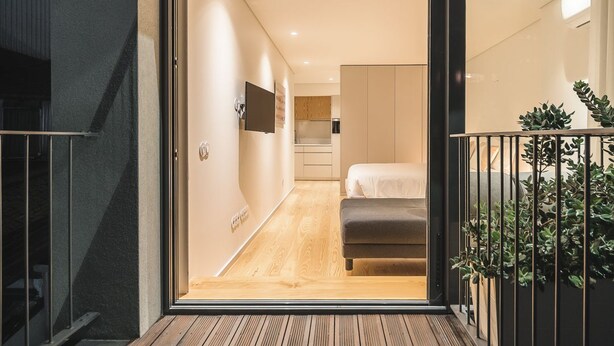 A modern interior with a wooden floor, a bed, a TV, and a staircase leading to an upper level. - Bom JardimApartments (Porto)