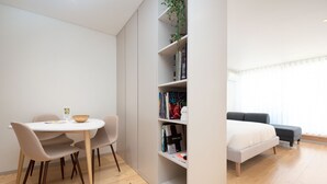 A modern, minimalist room with a dining table, chairs, a bookshelf, and a bed. - Bom JardimApartments (Porto)