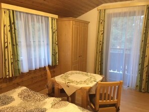 A room with a bed, a table with a tablecloth, a chair, a wardrobe, and large windows with curtains.