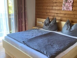A bed with a grey blanket and pillows, wooden headboard, and a window with curtains.