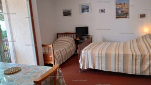 Een hotelkamer met twee bedden, een televisie, een tafel met bloemenlaken en een poster aan de muur.