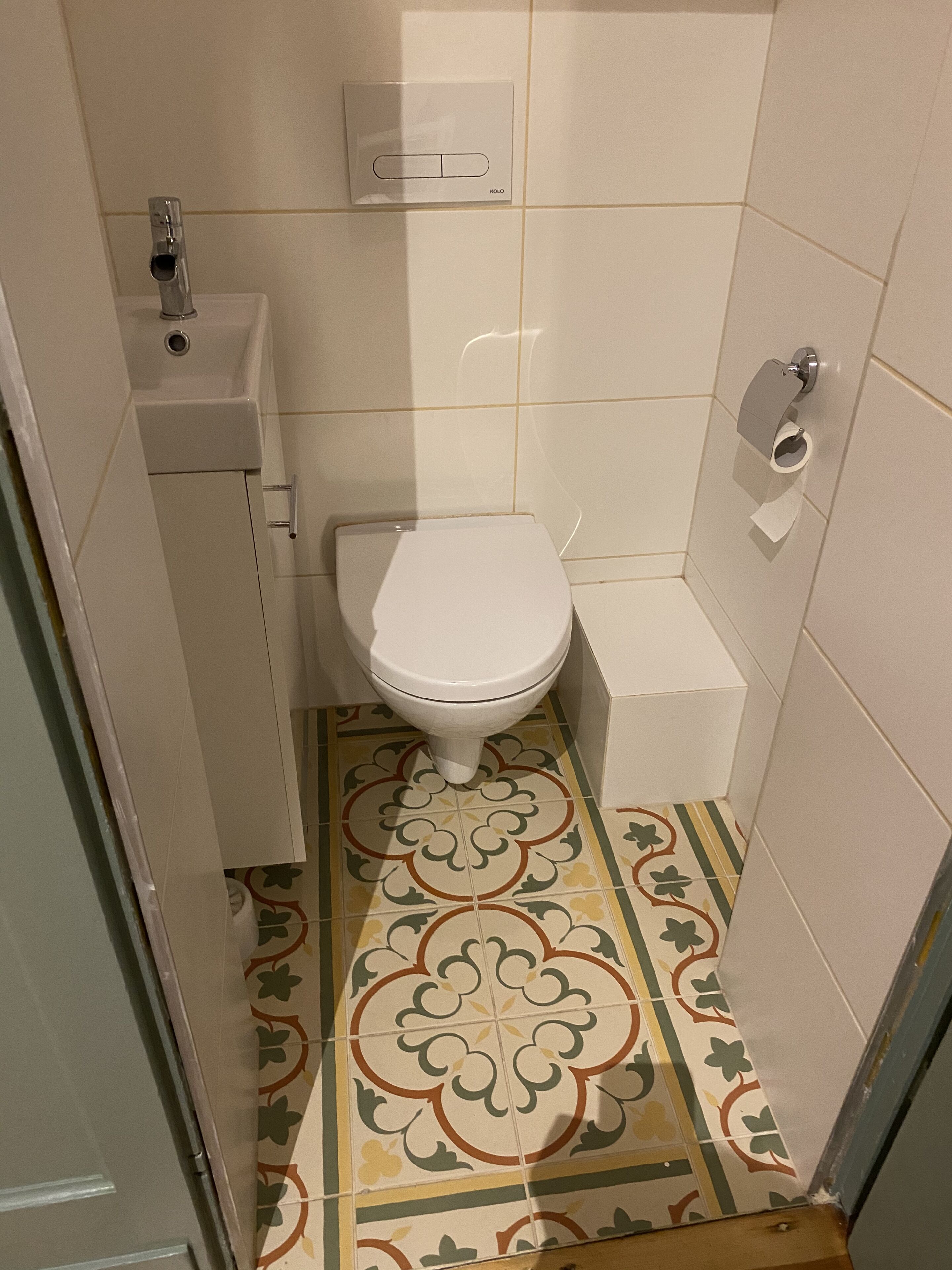A small bathroom with a toilet, a sink, and a toilet paper holder.