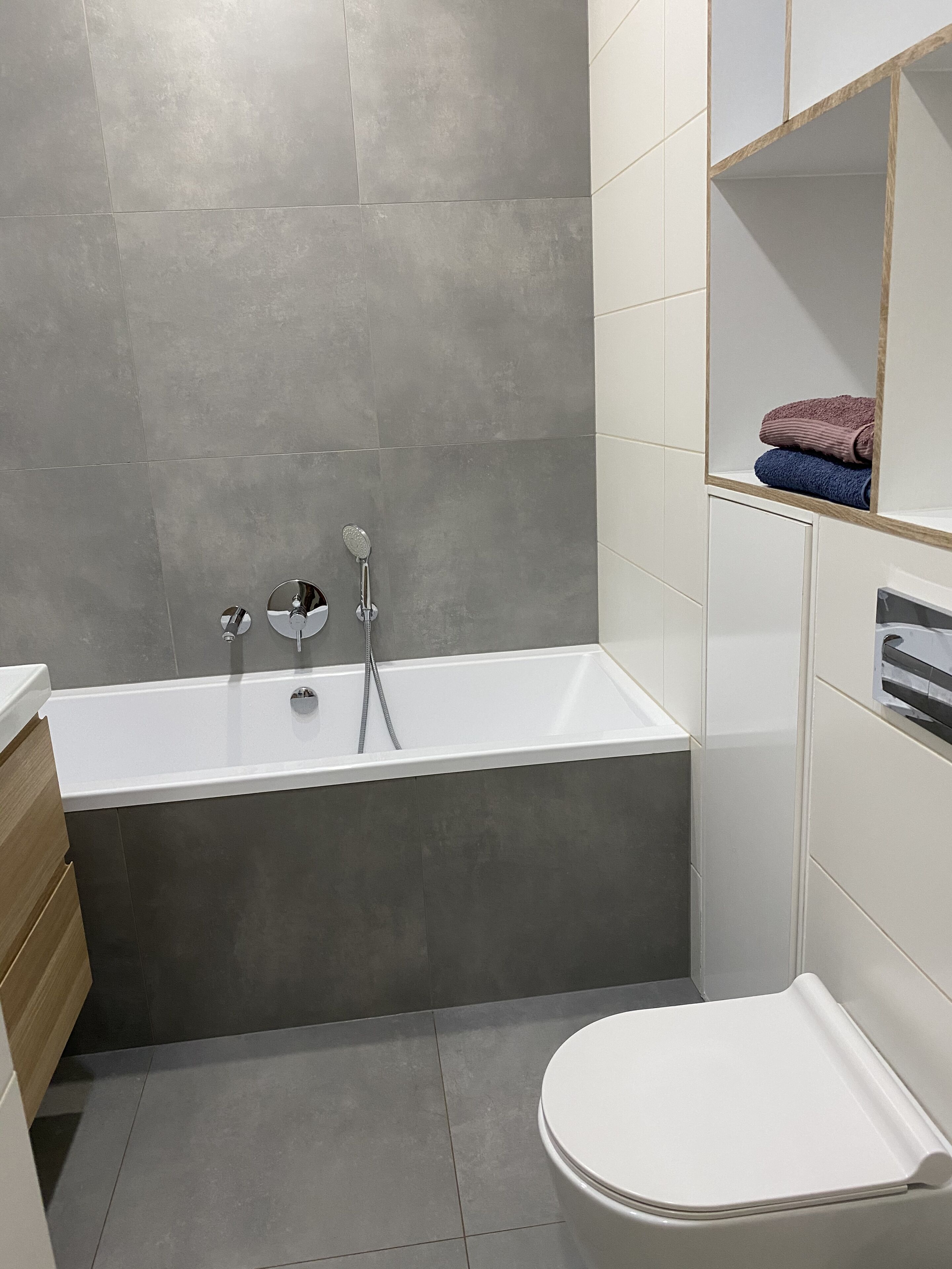A modern bathroom with a bathtub, a toilet, and a shelf with towels.