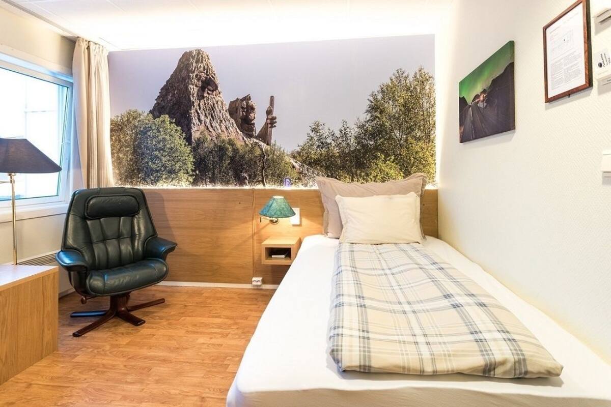 Una habitación pequeña y acogedora con cama, escritorio, silla, lámpara y un mural de un paisaje rocoso.