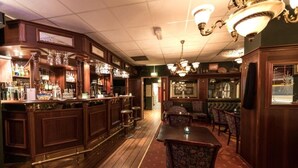 Zona de bar con mostradores de madera, taburetes y un área de estar con sillas estampadas.
