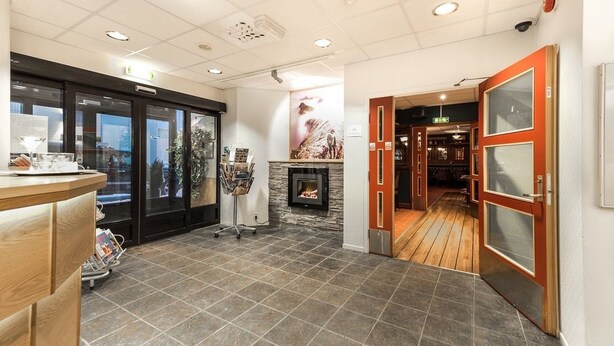 Un vestíbulo de hotel con una recepción, una chimenea y vistas al exterior a través de una puerta de cristal.