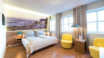 A hotel room with a bed, a yellow armchair, a small table, and a large window with curtains.