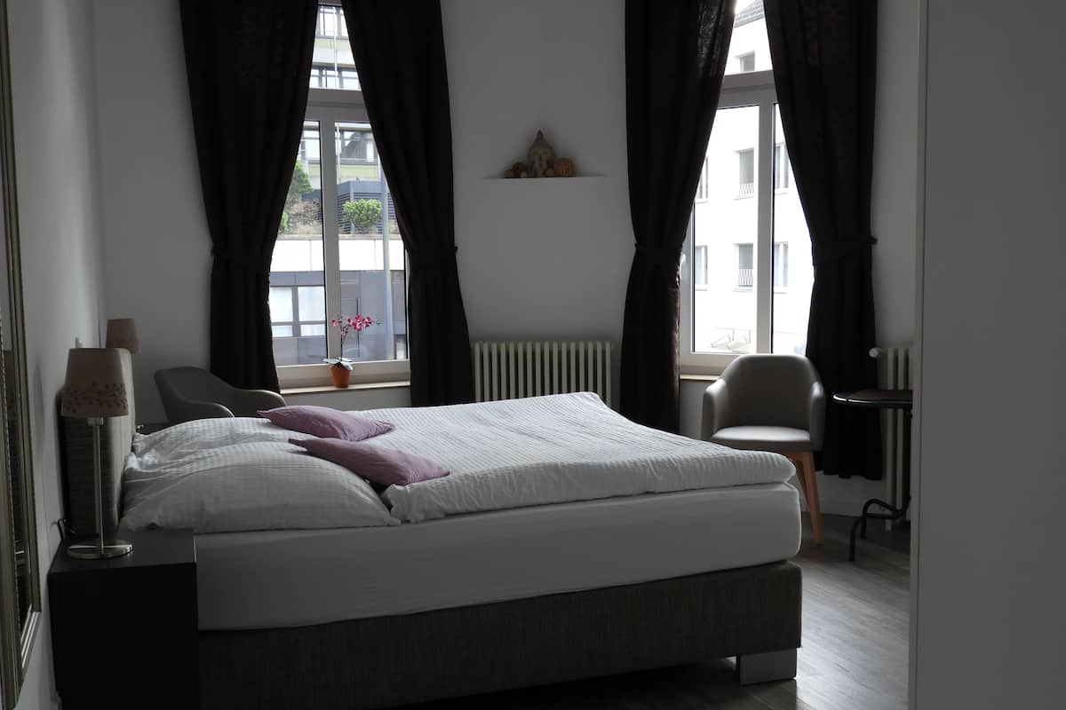 A bedroom with a bed, two chairs, a lamp, and a window with curtains.
