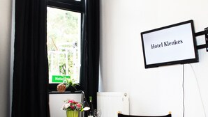 A hotel room with a bed, a desk with a computer, a chair, a window with black curtains, and a sign reading "Hotel Klernes". - Hotel Klenkes am Bahnhof (Aachen)