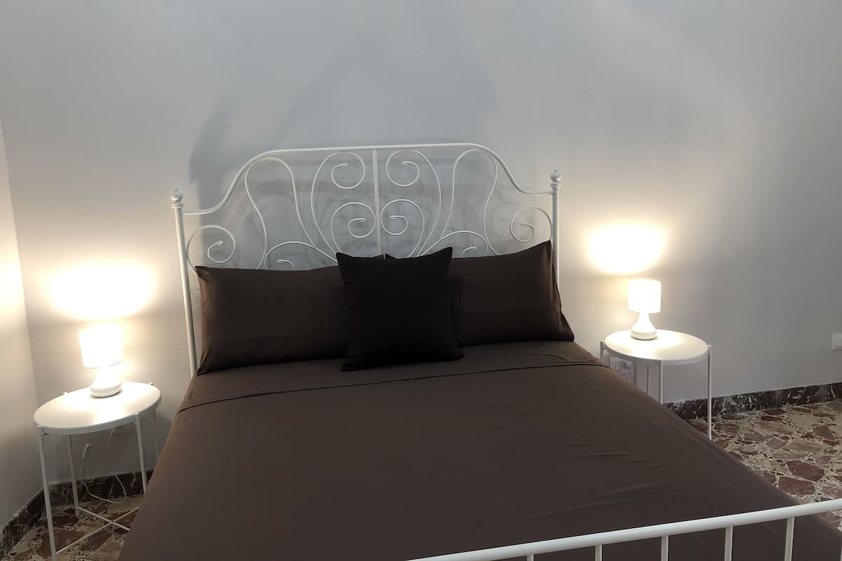 A neatly made bed with a metal headboard, two bedside lamps, and a marble-patterned floor.