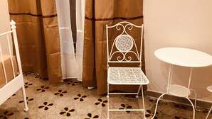A room with a patterned floor, a white metal chair, a small round table, and a curtain. - Meliora Rooms (Avola)
