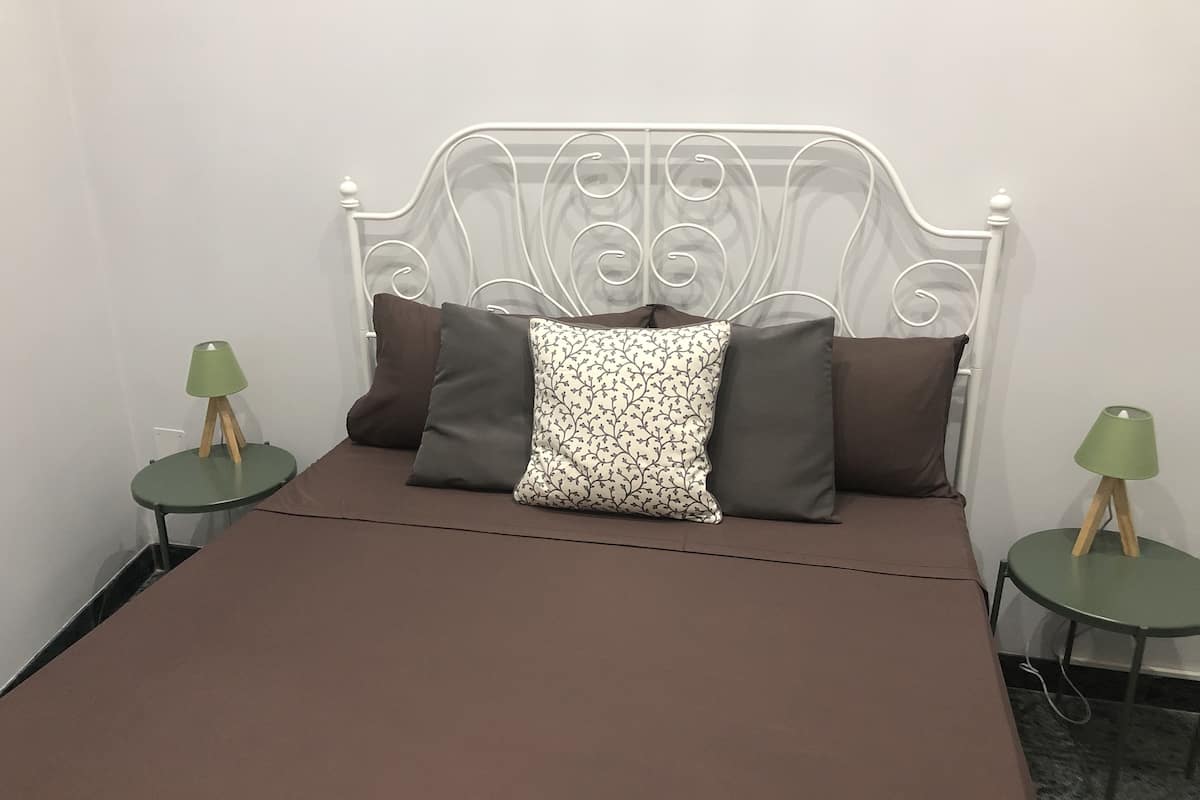 A bed with a white metal headboard, a brown bedspread, and two green nightstands with lamps.