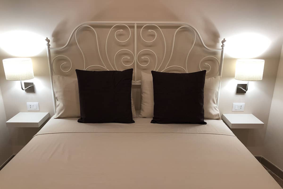 A neatly made bed with two black pillows, a white headboard, and two bedside lamps on matching nightstands.