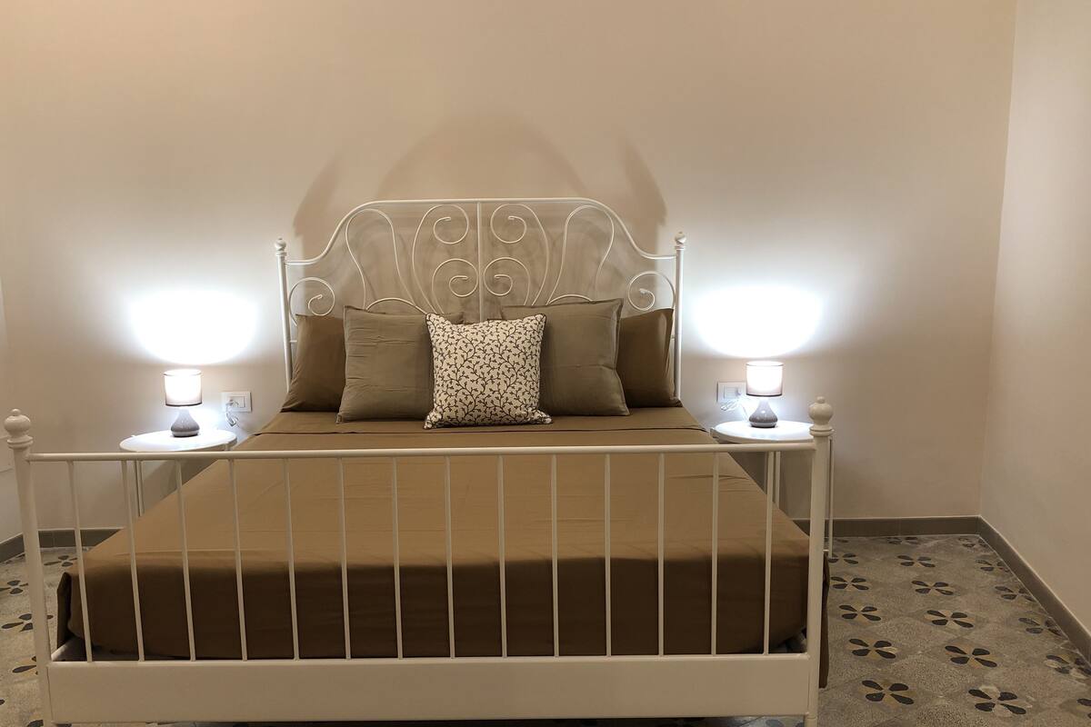 A bed with a metal frame, a headboard with a decorative design, and two bedside lamps.
