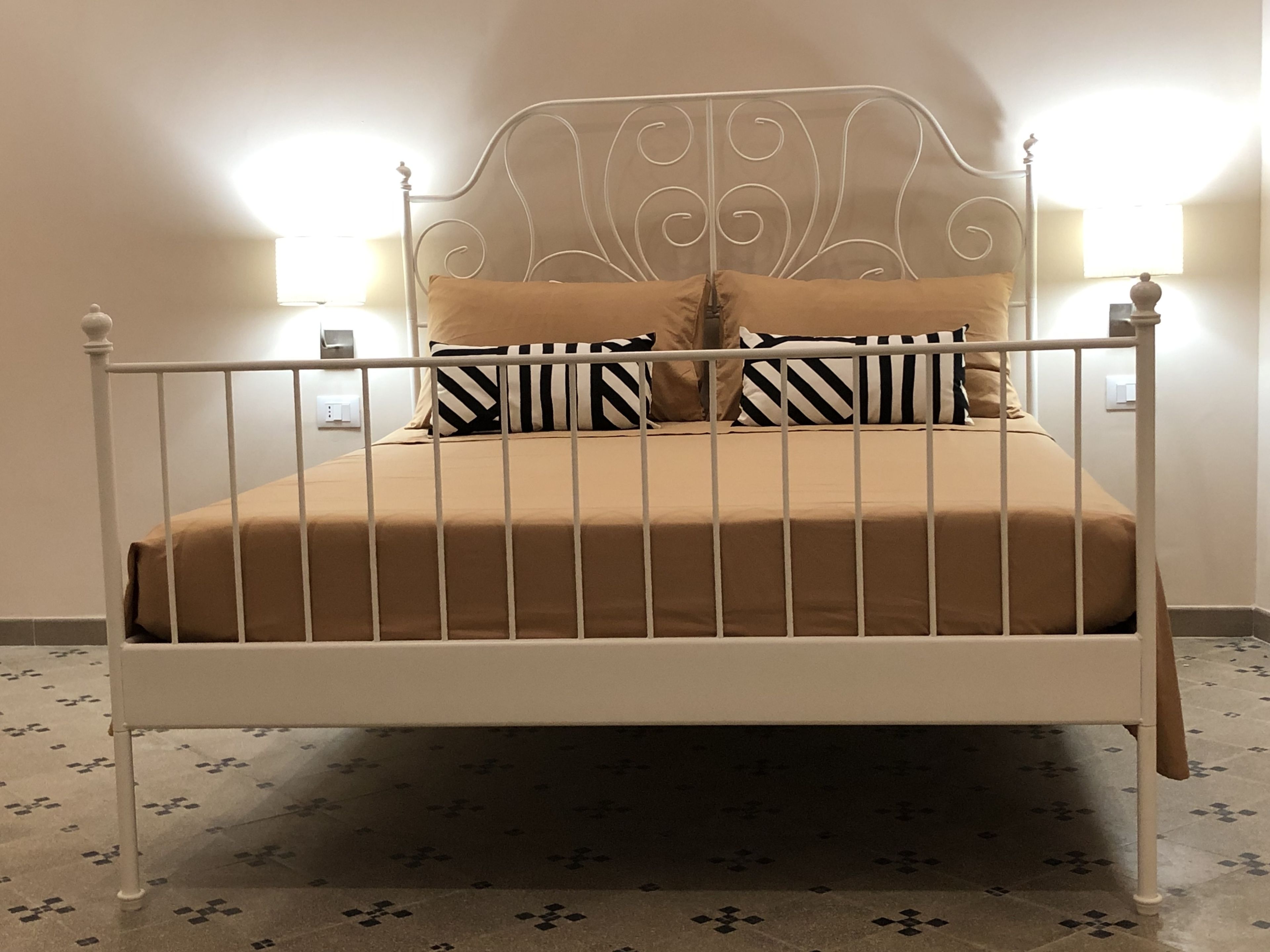 Un lit avec un cadre en métal, une literie de couleur beige et des oreillers à rayures.