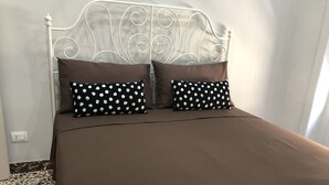 A bed with a white metal headboard, two brown pillows, and a brown bedspread. - Meliora Rooms (Avola)