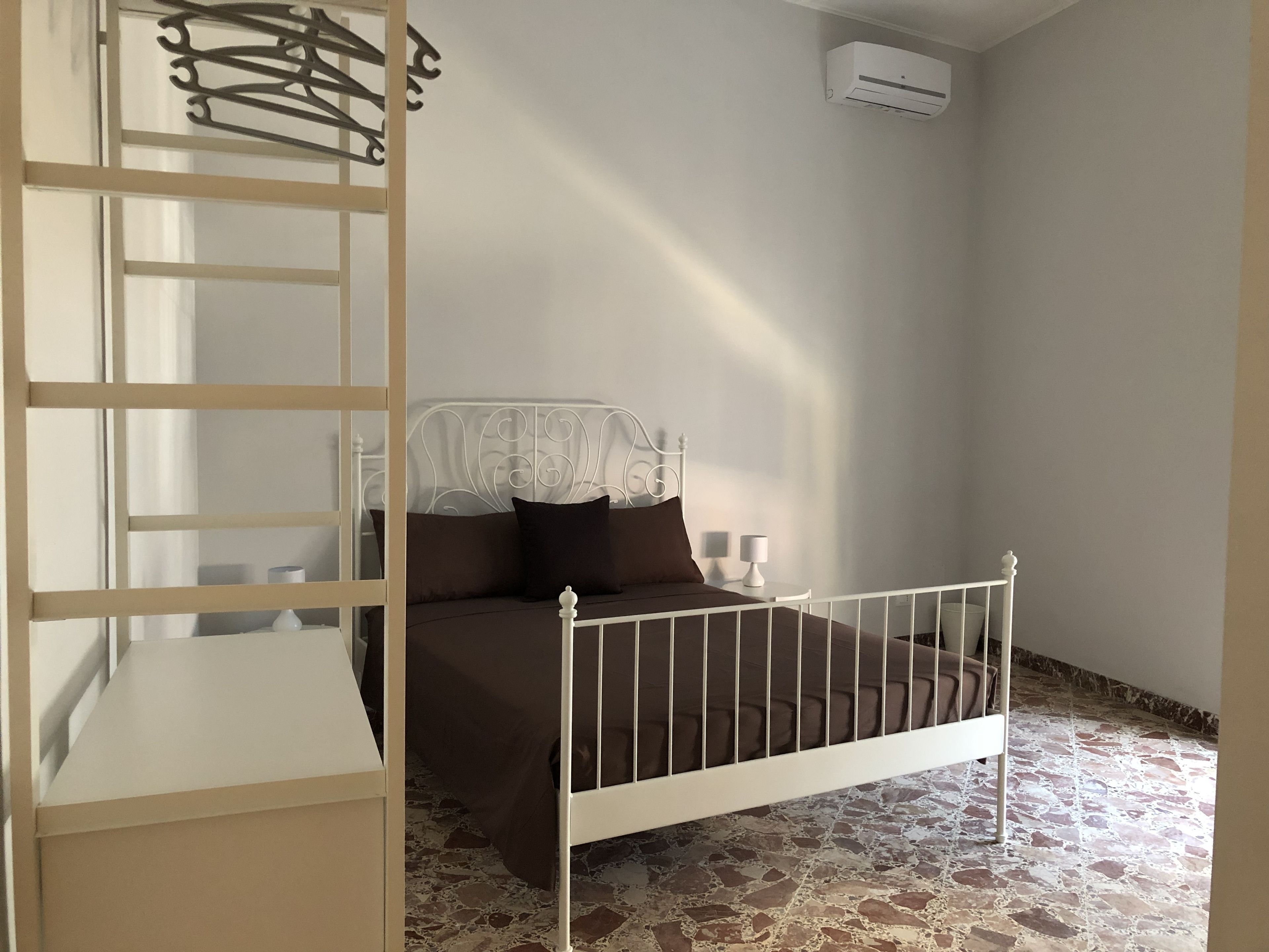 Ein Schlafzimmer mit Bett, Nachttisch, Lampe, Kleiderschrank und Klimaanlage.
