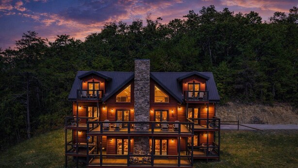 Una cabaña de troncos de dos pisos con una chimenea de piedra, varios balcones y una terraza con mobiliario exterior.