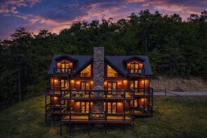 A two-story log cabin with a stone chimney, multiple balconies, and a deck with outdoor seating. - Amazing View Lodge- Breathtaking Views, 10 minutes to downtown Pigeon Forge! (Sevierville)