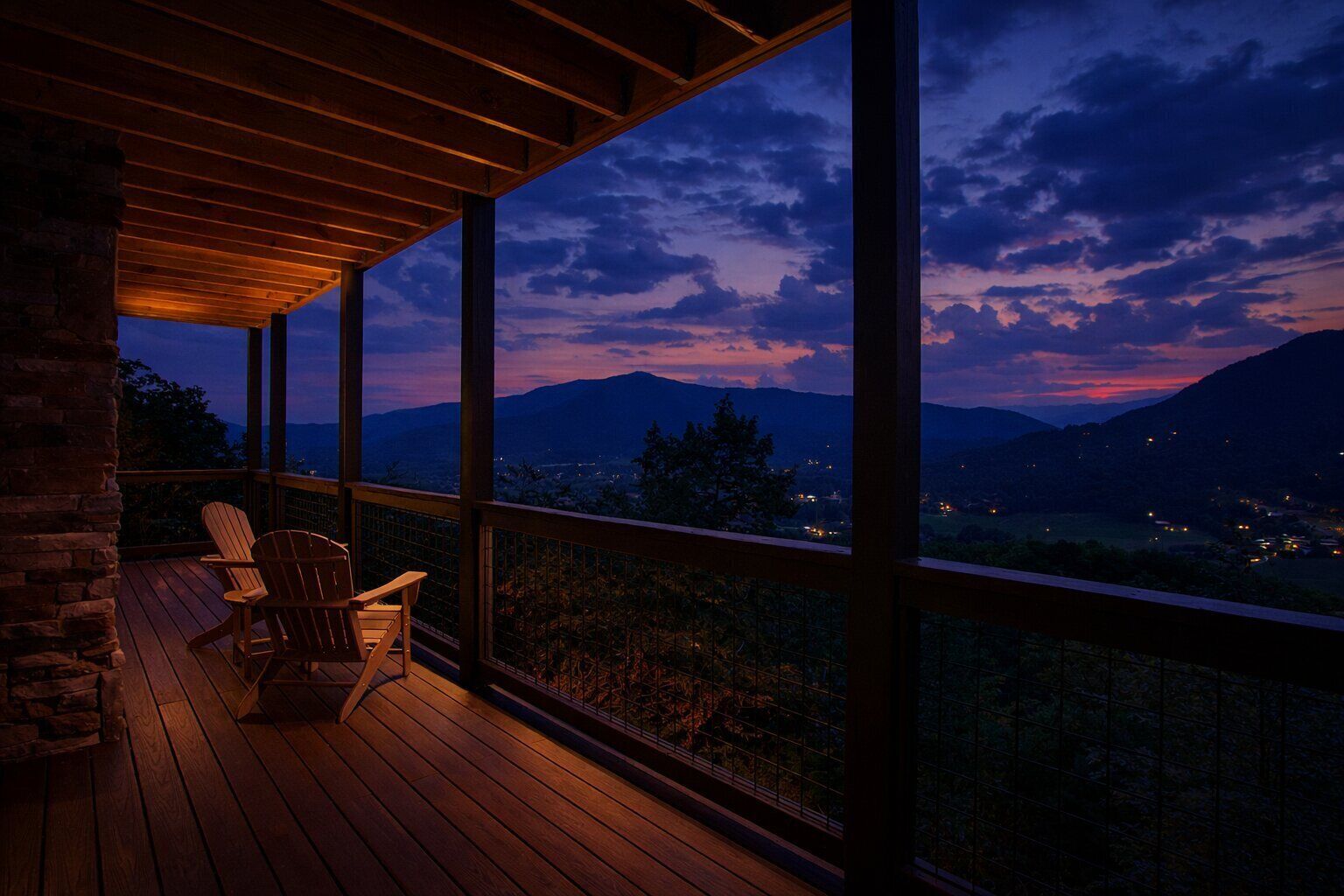 A wooden deck with chairs overlooking a mountainous landscape at dusk.
