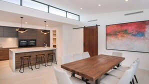 Eine moderne Küche mit einer zentralen Kochinsel, Barhocker und einem Essbereich mit einem Holztisch und weißen Stühlen.