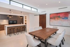A modern kitchen with a central island, bar stools, and a dining area with a wooden table and white chairs. - Marine Life—Coastal Retreat Near Busselton Jetty (Busselton)