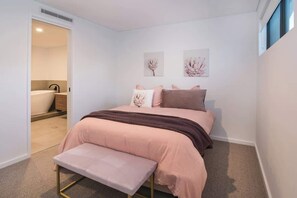 Una camera da letto con un letto, una panca, due opere d'arte appese al muro e un bagno in vista.