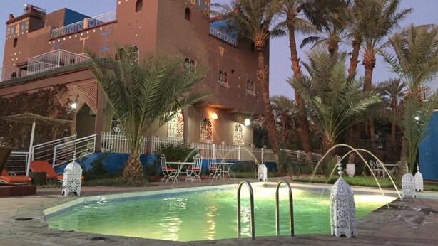 A pool area with a building in the background, palm trees, and outdoor seating.