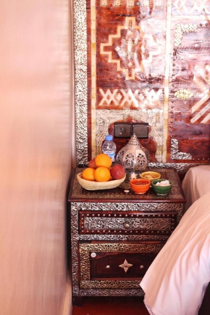 Habitación tradicional con cama, un muro decorativo y una mesita de noche con un frutero y una botella de agua.