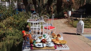 An outdoor dining table set with breakfast items, surrounded by greenery and a white metal chair.