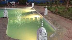 A courtyard with a swimming pool, palm trees, and a building with decorative lighting.