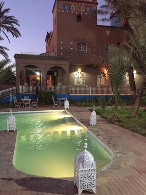 A courtyard with a swimming pool, palm trees, and a building with decorative lighting.