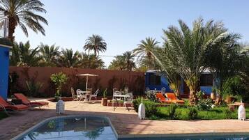A pool area with lounge chairs, a table, and chairs, surrounded by palm trees and a blue building.