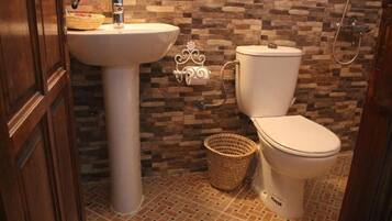 A bathroom with a stone wall, a white sink, a toilet, and a shower.