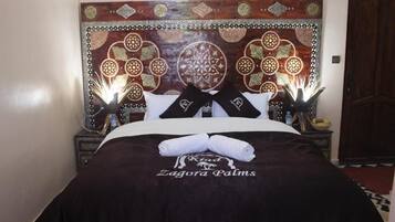 Un lit bien fait, avec une couverture sombre et deux oreillers, une tête de lit décorative ornée de motifs complexes, et une serviette posée sur le lit.
