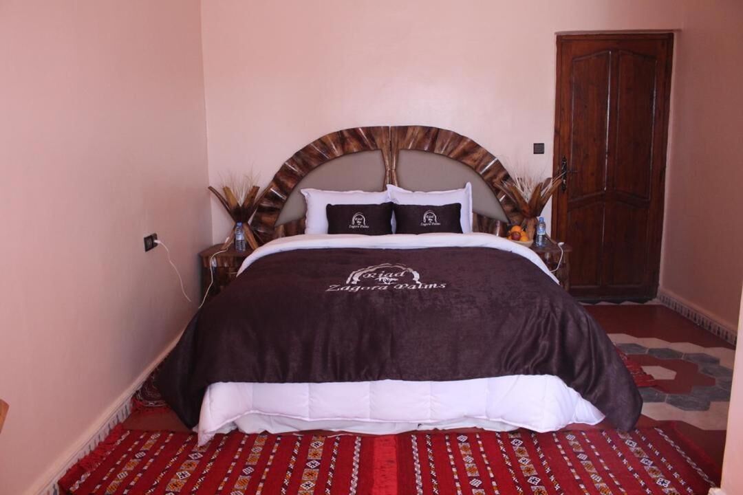 A bed with a brown and white bedspread, a wooden headboard, and a red patterned rug.