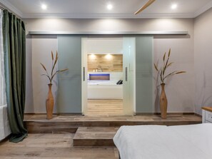 Un dormitorio moderno con una cama grande, un baño con tocador de madera y dos jarrones con plantas secas.