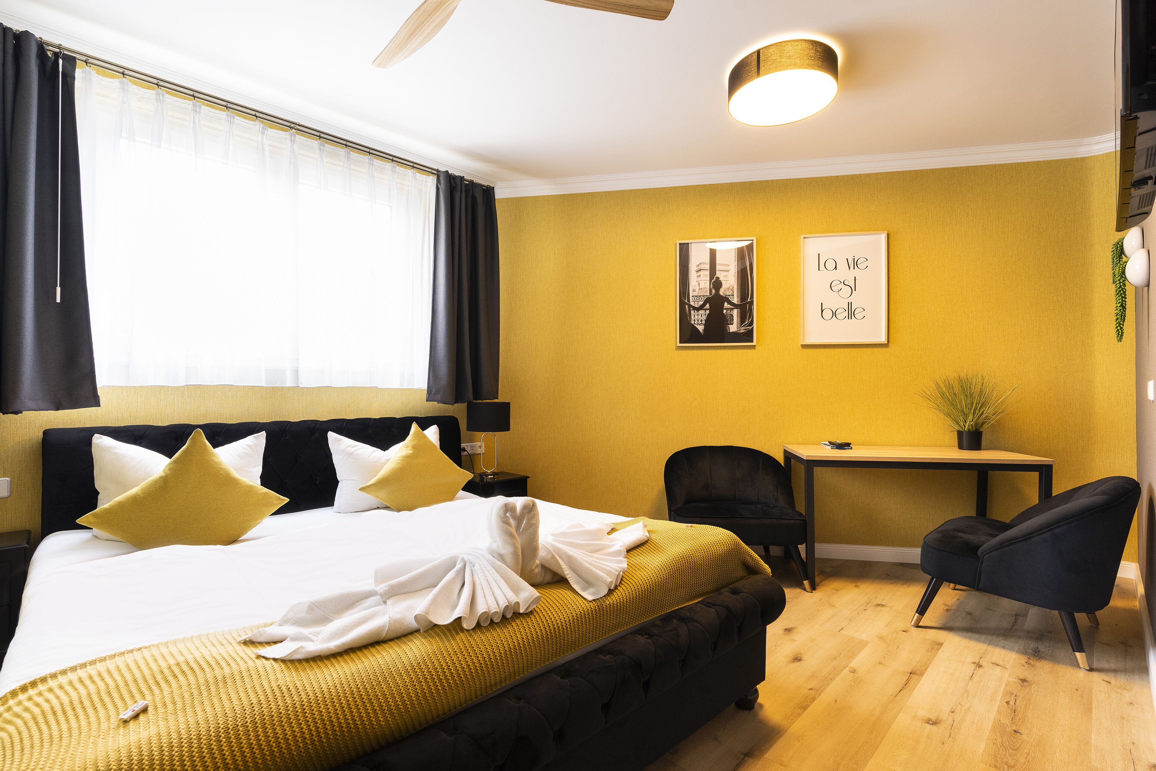 A hotel room with a bed, a desk, a chair, and two framed pictures on the wall.
