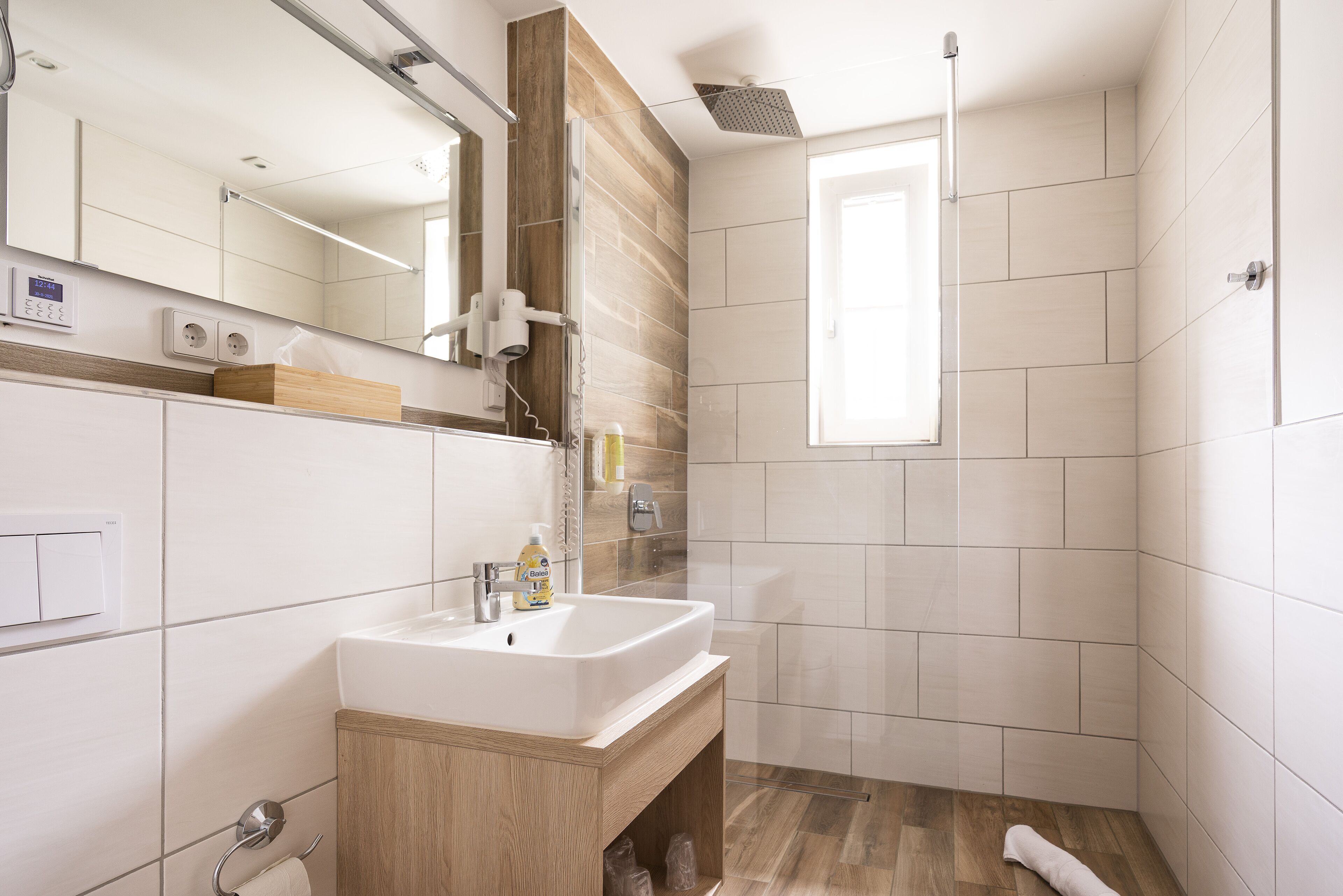 Ein modernes Badezimmer mit einem weißen Waschbecken, einer Holzkommode und einer Dusche mit Glastür.