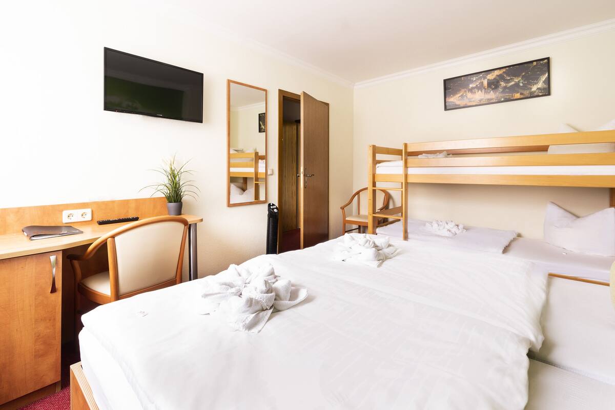 A hotel room with a bunk bed, a desk with a chair, a TV, and a mirror.