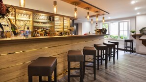 A bar area with a wooden counter, multiple stools, and hanging pendant lights. - Cityhotel Bernburg (Bernburg)